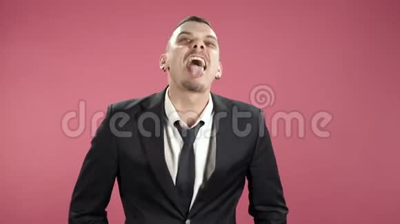 穿西装的年轻人在粉色背景下做鬼脸露出舌头视频的预览图