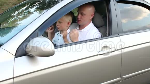 父子俩穿着白色t恤坐在车后的车轮上视频的预览图