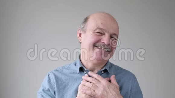 开朗的老年西班牙裔男子开心地微笑双手放在胸前表达他的积极情绪视频的预览图