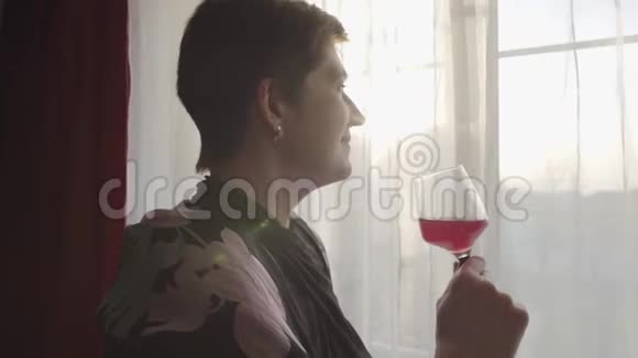 高加索族妇女手持酒杯向窗外看疲惫的微笑女士的肖像视频的预览图