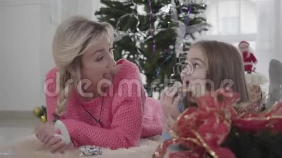 一个快乐的白人女孩和妈妈一起躺在地板上吃饼干可爱的金发母亲看着她视频的预览图