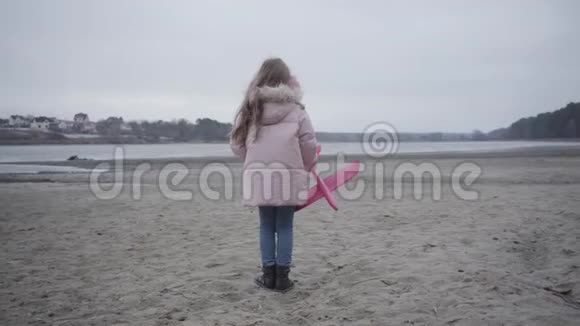 镜头接近身着粉色衣服戴着耳机的深黑色白种人女孩她站在河岸上迎风而举视频的预览图