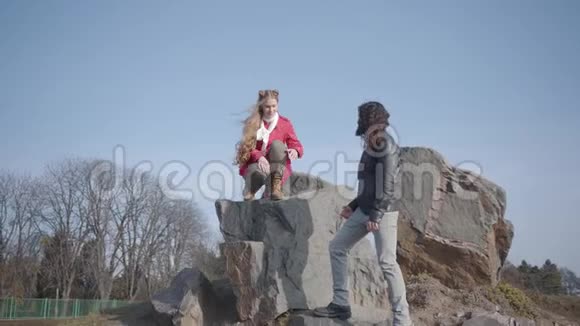 年轻的中东男人穿着休闲装帮助他可爱的高加索女朋友从岩石上下台时髦的嬉皮士视频的预览图