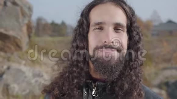 美丽的中东男人留着长长的黑发和胡须站在秋天公园微笑着视频的预览图