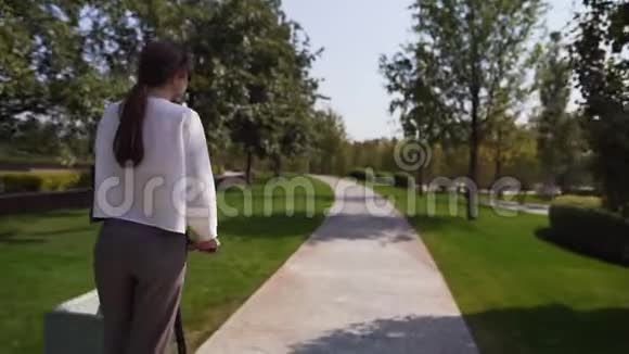 追踪射击一个穿着白色衬衫的年轻女孩正在一个温暖的夏天骑在绿色公园里趋势生态模式视频的预览图