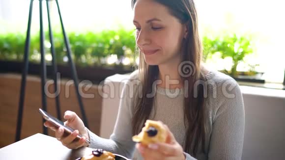 一个女人在咖啡馆里吃麦片用智能手机视频的预览图