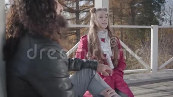 积极的年轻白人妇女坐在亭子里的长凳上与她的中东男朋友交谈的肖像视频的预览图