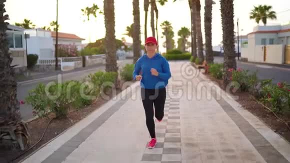 日落时女人沿着棕榈大道沿着街道跑健康的积极生活方式慢动作视频的预览图