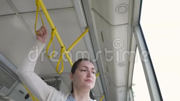 美丽的女人站在电车上手握扶手走向城市视频的预览图