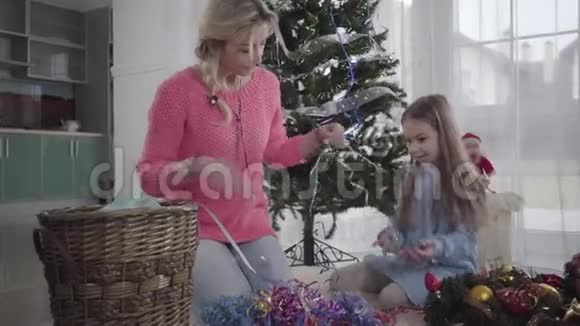 布鲁内特白种人女孩选择花环与妈妈坐在新年树的背景母亲和女儿视频的预览图
