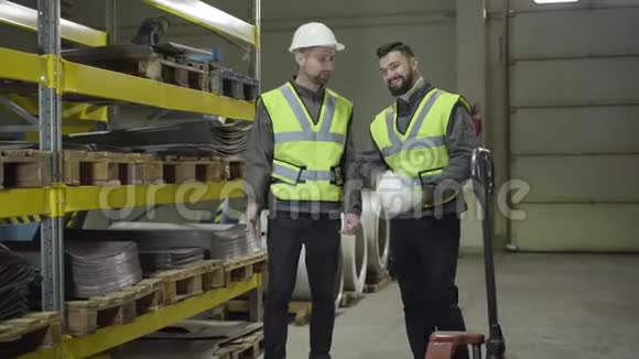 两个微笑的白种人站在钢铁金属仓库边说话在生产现场工作的工人视频的预览图