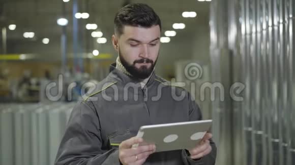 集中留胡子的白种人站在生产现场并使用平板电脑的肖像现代工头检查视频的预览图