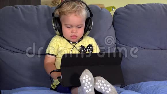 可爱的学步女孩带着耳机使用平板电脑和听音乐视频的预览图