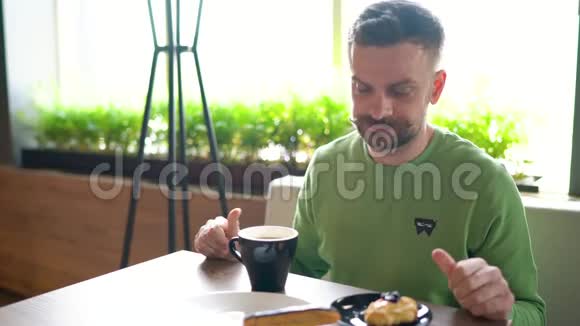 留着卷曲胡子的大胡子男人在咖啡馆里吃巧克力喝咖啡视频的预览图