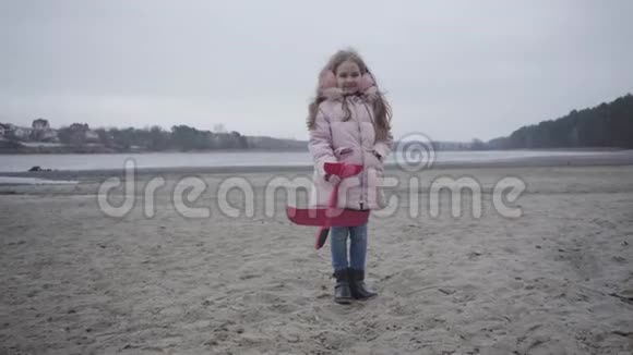 穿着粉红色外套和戴着耳机的白种人小女孩站在河岸上的玩具飞机的肖像儿童视频的预览图