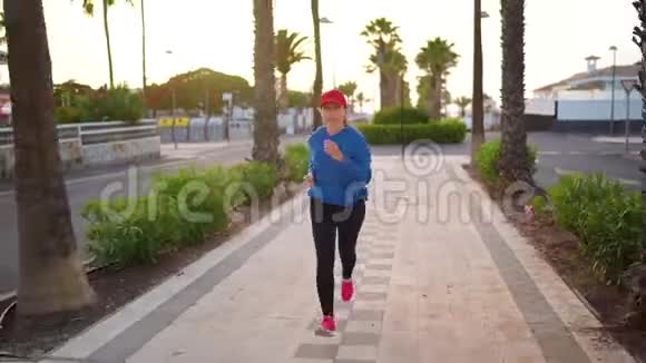 日落时女人沿着棕榈大道沿着街道跑健康的生活方式视频的预览图