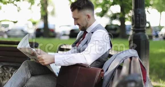 一个留着胡子的商人坐在公园里看报纸的特写视频的预览图