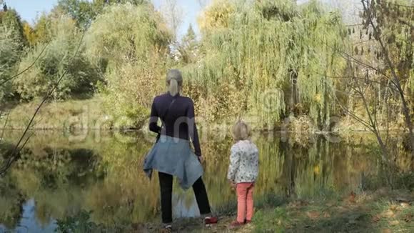 一个女人和一个小女孩站在河岸上在一个晴朗的秋天看着远处观点视频的预览图