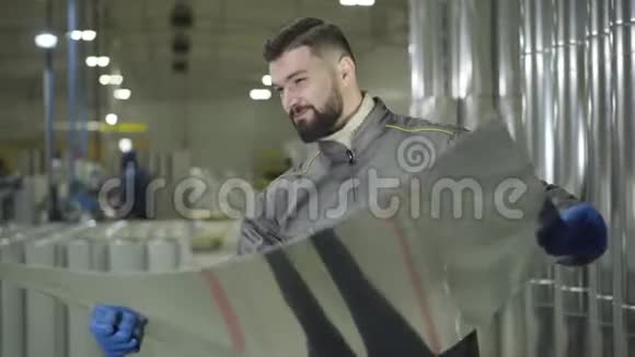 长胡子的白种人戴着工作手套站在金属钢管上拿着金属片年轻工人检查视频的预览图