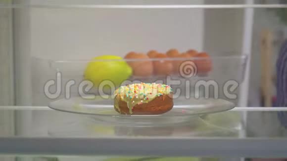 可爱的女人从冰箱里拿了一个美味的甜甜圈视频的预览图