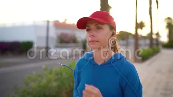 日落时女人沿着棕榈大道沿着街道跑健康的积极生活方式慢动作视频的预览图