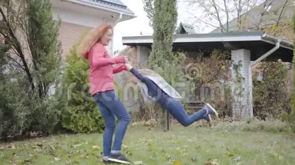 年轻的白人红发母亲在院子里纺女儿可爱的金发碧眼的小女孩视频的预览图