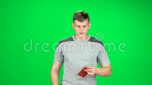 微笑的男人去摄影棚用绿色屏幕上的智能手机自拍视频的预览图