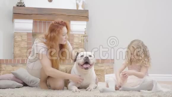 红发白种人的母亲和心烦意乱的金发女儿玩他们的狗成年妇女和小女孩带着宠物休息视频的预览图