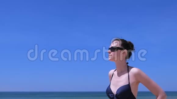 肖像女子日光浴站在海滩上穿着泳装在海天背景视频的预览图