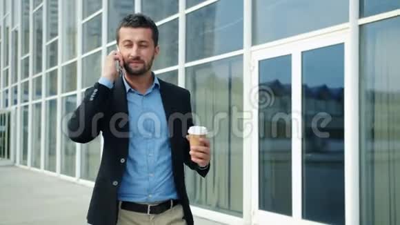 快乐的企业家走在城市里用手机拿着咖啡说话视频的预览图