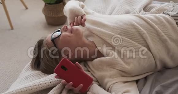 疲惫的女人在床上用手机伸展身体视频的预览图