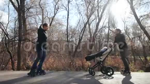 年轻的家庭轮滑带着一个婴儿在一个美丽的秋天公园的婴儿车里妈妈骑着车回去娱乐视频的预览图