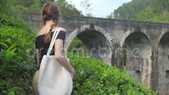 穿着黑色T恤的漂亮女孩沿着绿色种植园散步视频的预览图