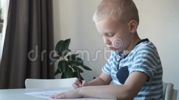 男孩孩子坐在家里的桌子上画画或做家庭作业视频的预览图