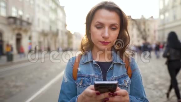 日落时分女人用智能手机走在老街上传播社交网络的概念慢动作视频的预览图