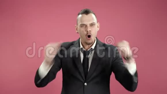 穿着西装的年轻时髦男士高兴地摆出赞成的姿势在粉红色的背景上拍手视频的预览图