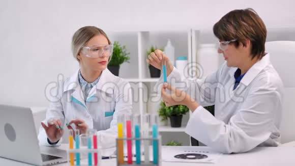 两位女医学家使用笔记本电脑在试管中使用彩色液体物质视频的预览图