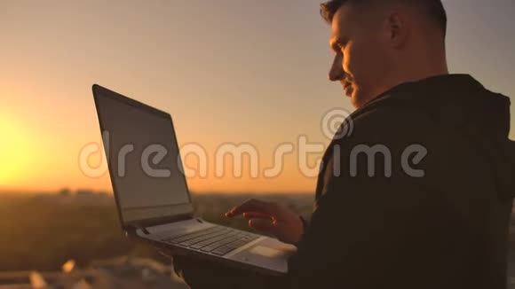 特写一个程序员在日落时分手在笔记本电脑键盘上打字俯瞰屋顶一个商人在远程工作视频的预览图