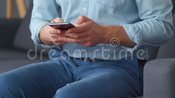 穿着正式的男人坐在沙发上用智能手机发短信特写视频的预览图