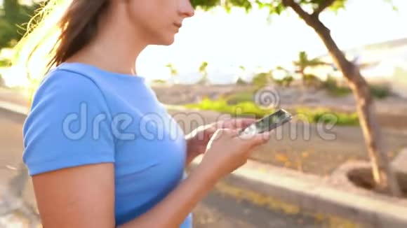 穿着蓝色连衣裙的女人用智能手机站在热带风景的街道上视频的预览图