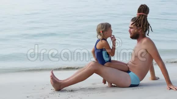 女儿和父亲坐在海边的沙滩上女孩说爸爸的牙齿有东西卡住了视频的预览图