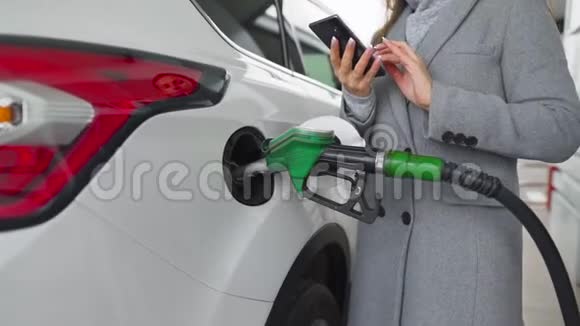 女人在智能手机上打短信而她的车在加油视频的预览图