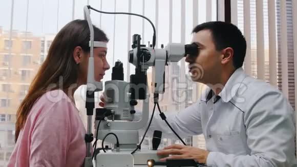 眼科治疗一位医生用一台大的验光机检查年轻女性的视力一个宽敞的房间视频的预览图