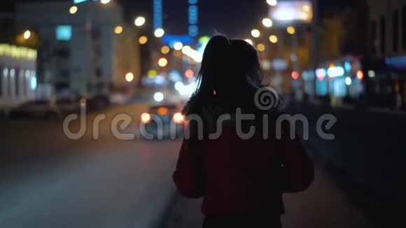 年轻女子走在城市的马路上经过过往车辆的灯光视频的预览图