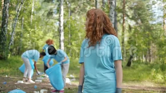 年轻女性生态活动家在森林里微笑而团队收集垃圾的肖像视频的预览图