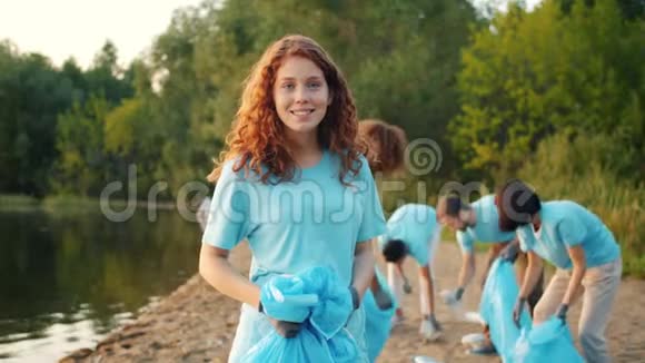 美丽的女志愿者在海滩上看镜头同时团队打扫视频的预览图