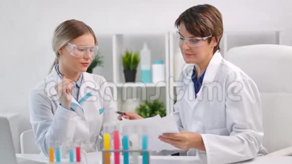 两名女化验员戴着制服和防护眼镜在实验室里看着文件视频的预览图