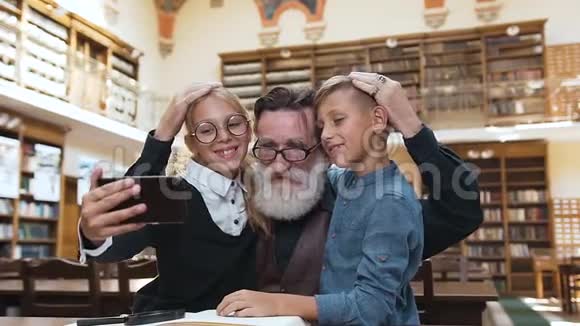 一位戴眼镜的英俊留胡子的快乐男子在用女孩的手机自拍时拥抱了他微笑的12个孙子视频的预览图
