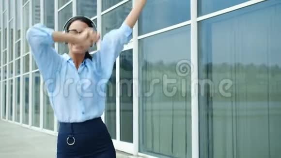 在街边的办公中心外面跳舞的商务小姐戴着耳机视频的预览图