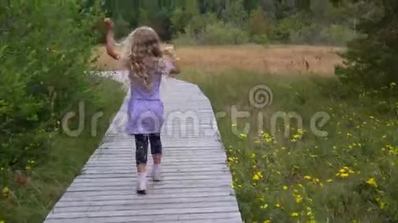 穿着紫罗兰色衣服的小女孩独自走在木路上视频的预览图